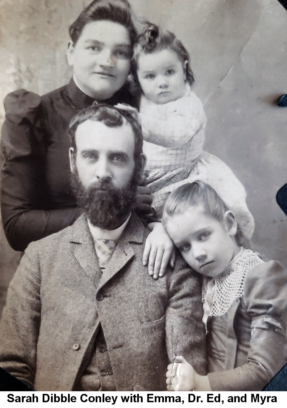 IMAGE/PHOTO: Sarah Dibble conley with daughter Emma, husband Dr. Ed, and daughter Myra: Black and white photo Sarah Dibble Conley, holding toddler Emma, standing behind a seated Dr. Ed, on whom is leaning Myra Conley with a sad expression.